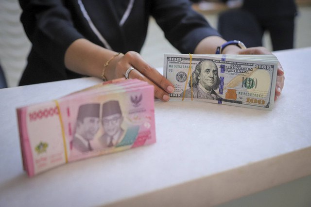 Seorang petugas menunjukan pecahan Dolar AS dan Rupiah di kawasan Kwitang, Jakarta, Senin (18/11/2024). Foto: Iqbal Firdaus/kumparan